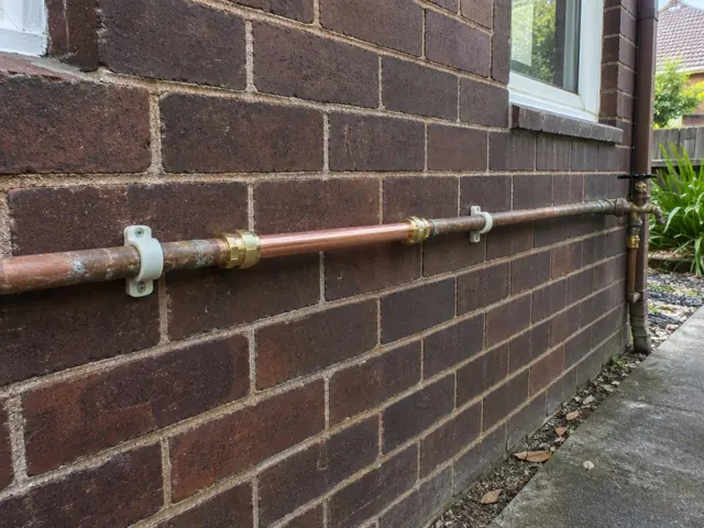 Repaired copper water pipe along a brick exterior wall beside a window in Normanhurst